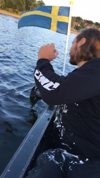 Guy in black sweatshirt on boat chugs beer and hand falls off into water 